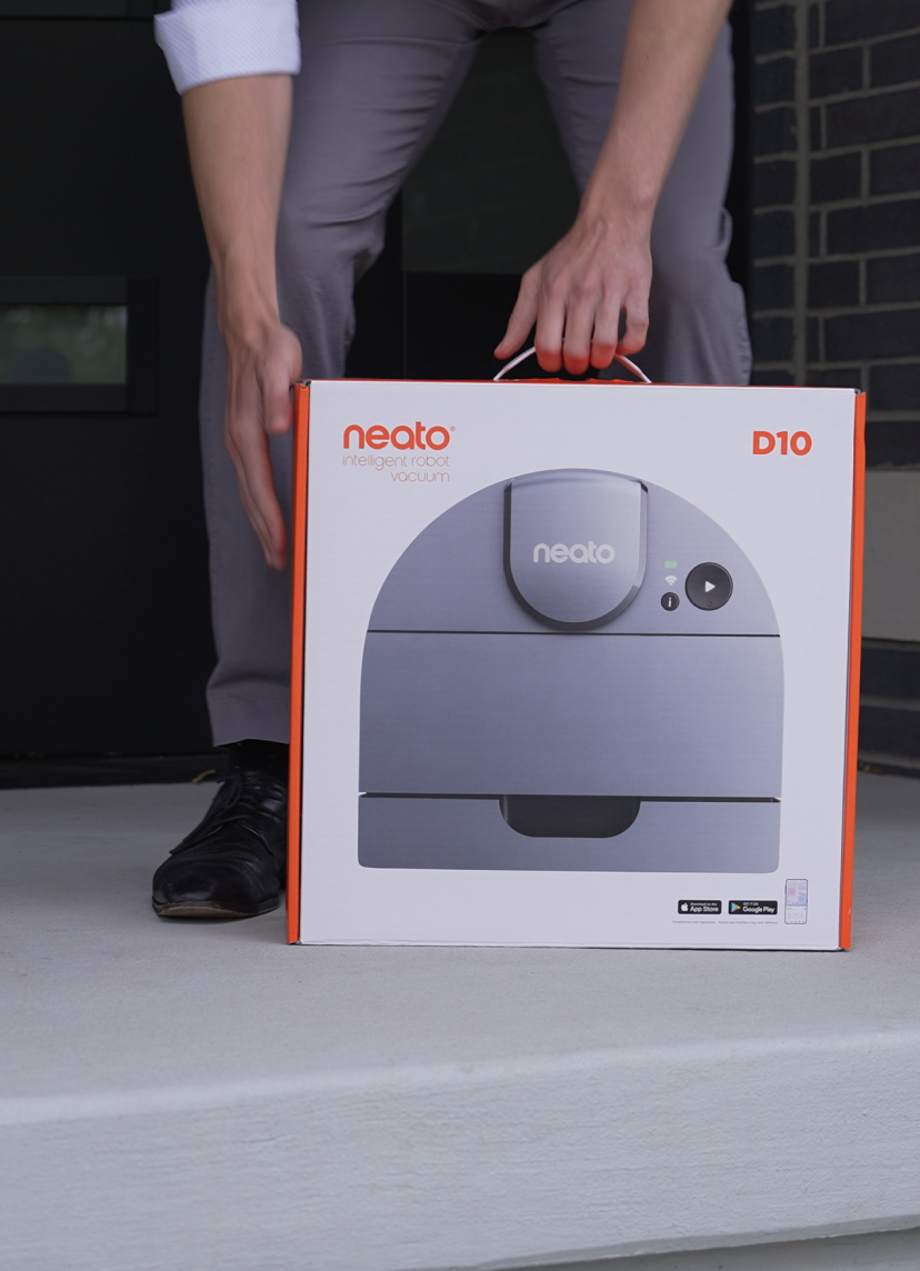 A man picking up a Neato Robotics vacuum in the packaging.