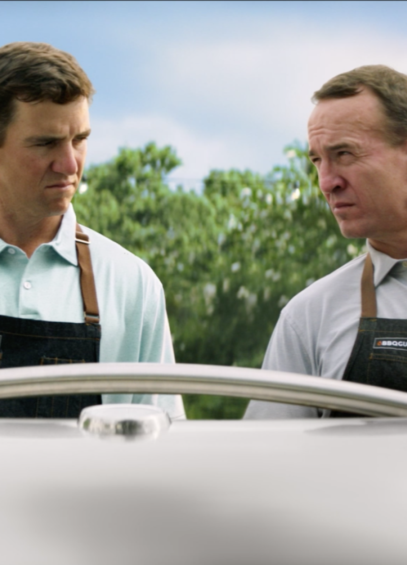 Eli and Peyton Manning looking over a grill.